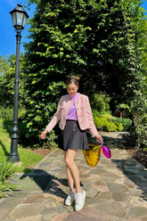 a lady in a purple top, a pink tweed jacket and a grey pleated skirt